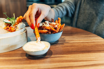 Woman dipping sweet potato fries into creamy sauce at a cozy restaurant