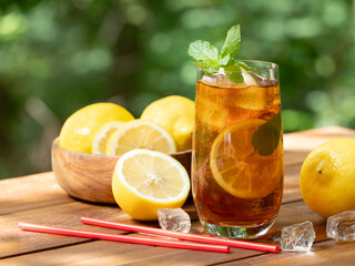 Glass of ice tea with lemon slices and mint outdoors on wooden table
