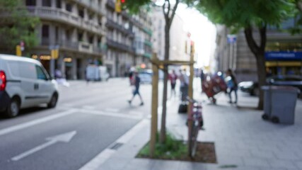 Blurry city street scene in barcelona, spain, showcasing defocused pedestrians, traffic, and urban life under soft sunlight.