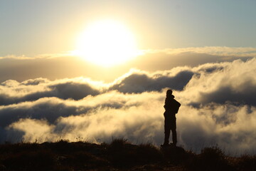 silhueta de homem caminhando em montanha com mar de nuvens ao fundo - foto tirada em santa...