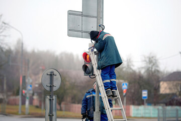 Electrician standing on ladder repair traffic light. Worker fixing traffic light at busy...