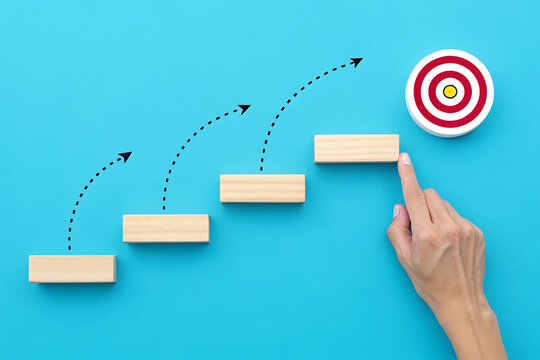 Conceptual image of stepping blocks and hand pointing to target goal, symbolizing progress, growth, and achieving success