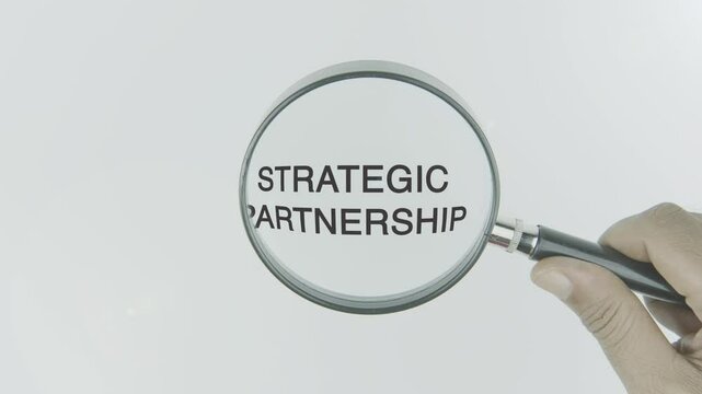 Strategic partnership text or word highlighted by a magnifying glass in a hand on a white background, symbolizing focus on collaboration, shared goals, and mutually beneficial alliances