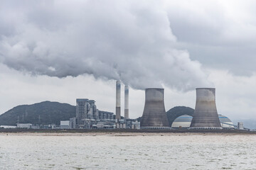 A thermal power plant in operation by the seaside, with chimneys emitting white smoke