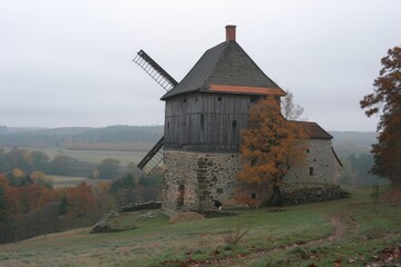 Fototapeta premium A large windmill is on a hillside with a stone house in the distance
