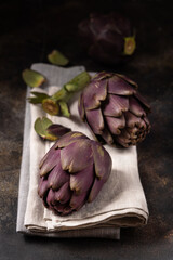 Head of purple raw romanesco artichokes on napkin on dark table closeup. Fresh italian vegetables