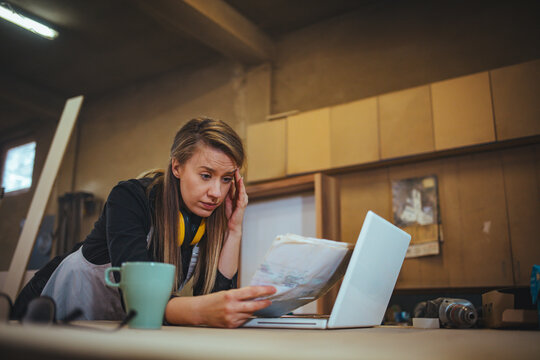 Focused Woman Analyzing a Document in Her Workshop Using Laptop