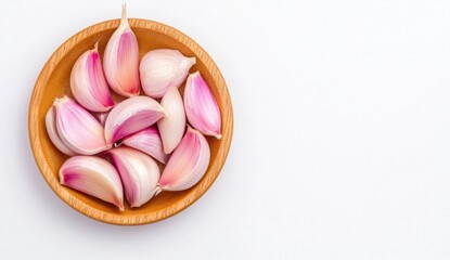 Overhead close up shot of peeled garlic cloves in a light brown wooden bowl on a white background. The garlic is pinkish white and shows natural variations in color and shape.