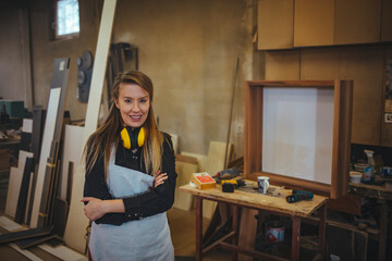 Confident Female Carpenter Standing in Workshop With Tools and Supplies Nearby