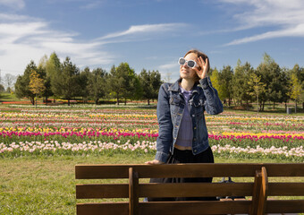 Happy woman in sunglasses posing in flower park. Enjoying walk, feeling good. Traditional tulip...