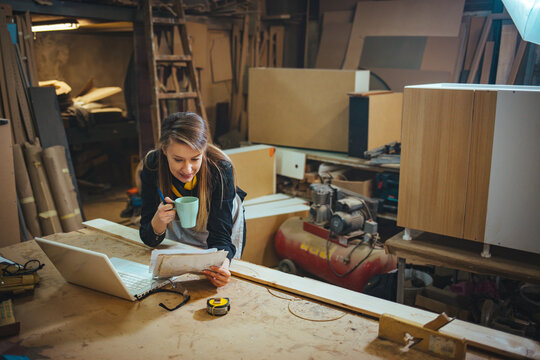 Young Woman Working on Laptop in a Creative Woodworking Workshop
