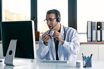 Male doctor explaining medical treatment to patient through a video call with laptop and earphones...