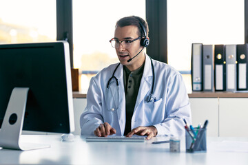 Male doctor explaining medical treatment to patient through a video call with laptop and earphones...