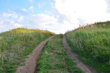 Dirt road winding up a grassy hill under a cloudy sky
