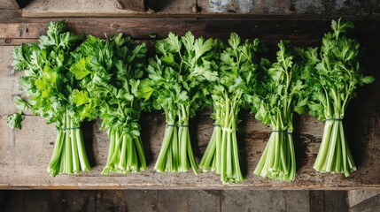 Five bundles of fresh green celery stalks on a rustic wooden surface