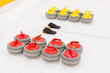 Two sets of curling stones of different colors for two teams, placed near concentric rings on an ice rink