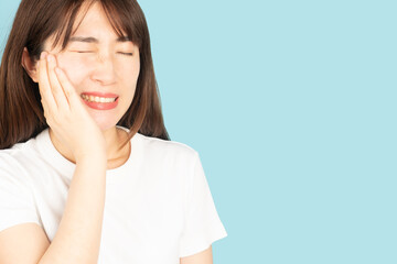 Asian woman suffering from toothache or jaw pain over blue background. Cause of painful included...
