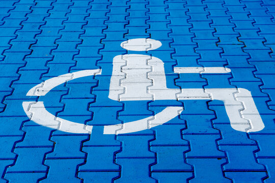 A bright blue pavement features a white accessibility symbol, clearly marking the area for wheelchair users in a public space during daylight - Powered by Adobe