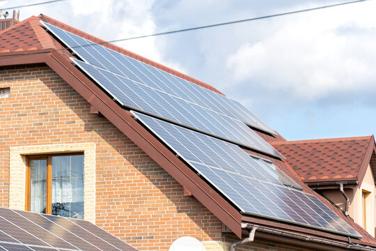 Solar panels covered the roof of a brick house under a bright blue sky, showcasing renewable energy use in the suburb