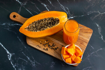A halved papaya, vibrant smoothie in a glass jar with a straw, fresh cubes in a bowl, and scattered...