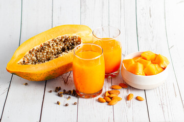 A halved papaya, vibrant smoothie in a glass jar with a straw, fresh cubes in a bowl, and scattered...