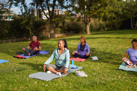 Group of multiracial senior people doing yoga meditation at city park during spring season - Healthy elderly lifestyle and mindfulness concept