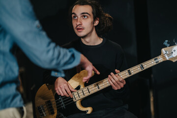 Obraz premium A young musician rehearses with a bass guitar while collaborating with a band mate in preparation for a concert. The setting reflects a music studio or rehearsal space atmosphere.