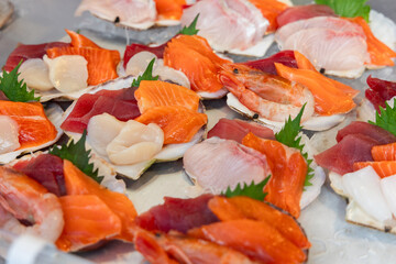 Assortment of fresh sashimi including salmon tuna shrimp scallops and white fish is elegantly arranged on scallop shells with shiso leaves at a seafood market in Tokyo for tasting