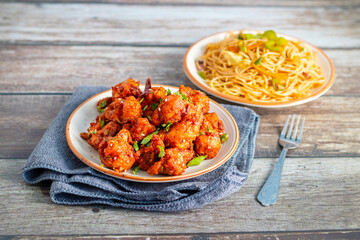 Crispy Gobi Manchurian coated in spicy, tangy sauce, served alongside stir-fried noodles with veggies, garlic, and soy flavors. A delicious Indo-Chinese delight!