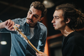 Two young men preparing for a band practice session, focusing on adjusting the guitar's tuning for optimal performance. The scene showcases dedication, teamwork, and their passion for creating music.
