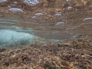 Dark blue ocean surface seen from underwater. Abstract waves underwater and rays of sunlight shining through, Sun light rays undersea deep, Underwater background with sea bottom, Mediterranean sea.