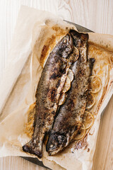 Baked trout fishes on wax paper on wooden table