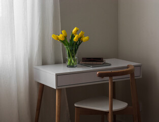 A cozy workplace - a bouquet of yellow tulips, a laptop, a notebook on a white table