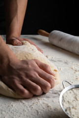 Male hands making dough for pizza, bread, pasta. Cooking bread. Kneading the Dough. Isolated on dark background. Copy space, production of flour products