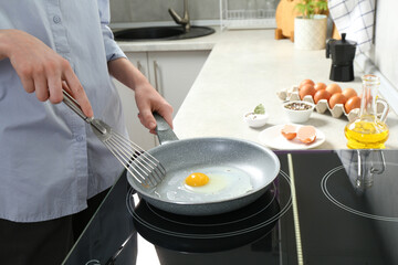 Woman with slotted turner cooking egg in frying pan on cooktop indoors, closeup