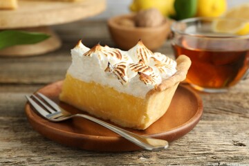 Piece of delicious pie with browned meringue and fork on wooden table, closeup