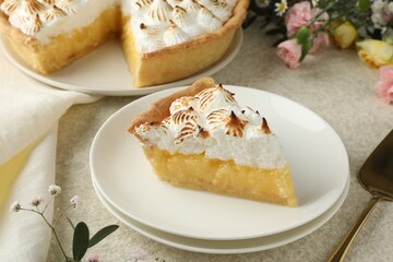 Piece of delicious pie with browned meringue and flowers on light textured table, closeup