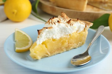Piece of delicious pie with browned meringue, spoon and slice of lemon on white wooden table, closeup