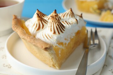 Piece of delicious pie with browned meringue and fork on light blue table, closeup