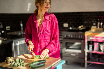 A woman in a relaxed home atmosphere prepares fresh vegetables on a rustic wooden table, bathed in warm natural light. A representation of slow living, wellness, and mindful daily rituals