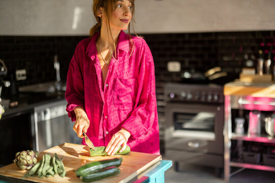 A woman in a relaxed home atmosphere prepares fresh vegetables on a rustic wooden table, bathed in warm natural light. A representation of slow living, wellness, and mindful daily rituals