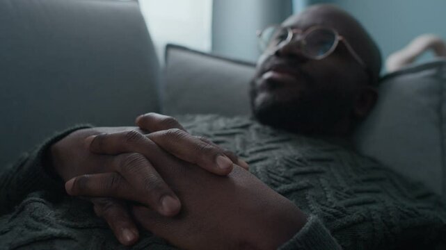 Selective focus shot of Black man with glasses gesticulating speaking about his past experiences when lying on couch during mental health consultation