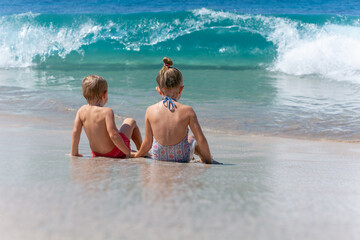 Happy kids have fun in sea surf on white sand beach. Couple of children sit in water. Travel lifestyle, swimming activities in family summer camp. Vacations on tropical island.