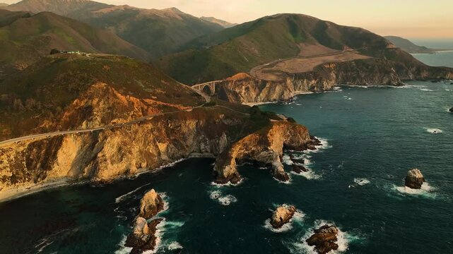 Aerial view of bixby creek bridge at sunset with fog over rugged cliffs and the ocean, Big Sur, California, United States.