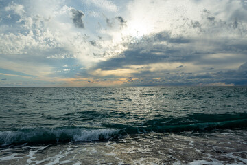 Fototapeta premium The sound of sea waves crashing on a pebble beach. The setting sun hid behind dark clouds.