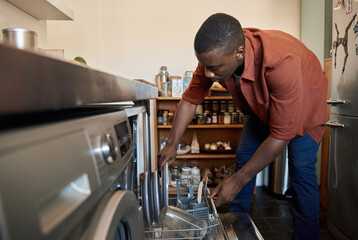 Young African man putting plates in his dishwasher at home