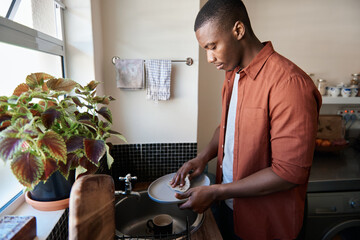 Young African man washing dishes in his kitchen sink at home