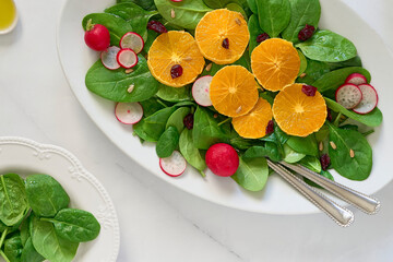 A top view of a salad on a ceramic plate consisting of spinach leaves, oranges, sunflower seeds and radishes. Top view, studio shot. Healthy vegan lunch, dinner concept.                           