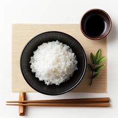 Culinary Harmony: A top-down shot captures a bowl of fluffy white rice, meticulously arranged on a bamboo mat alongside a small dish of dark sauce and a set of chopsticks.