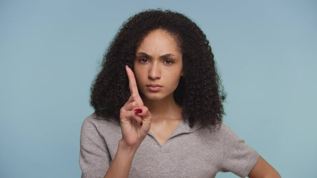 Serious woman pointing finger in warning gesture on blue background